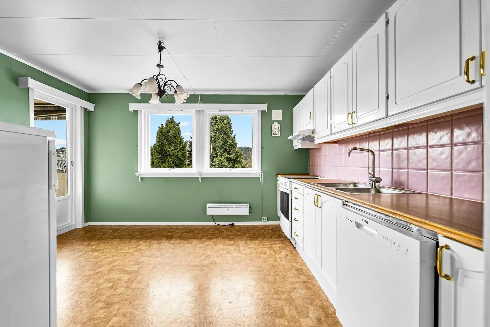 Innredningen har hvite, profilerte fronter og laminert benkeplate med nedfelt oppvaskkum i rustfritt stål. Det er flislagt mellom over- og u