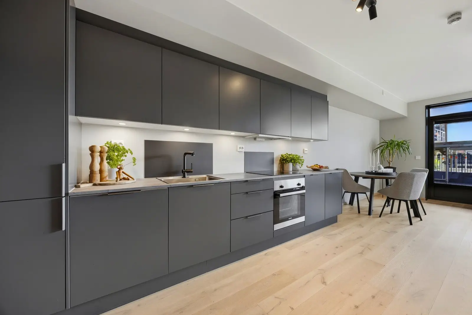 Moderne Sigdal-kjøkken med mørke glatte fronter og laminat benkeplate med nedfelt oppvaskkum i rustfritt stål.