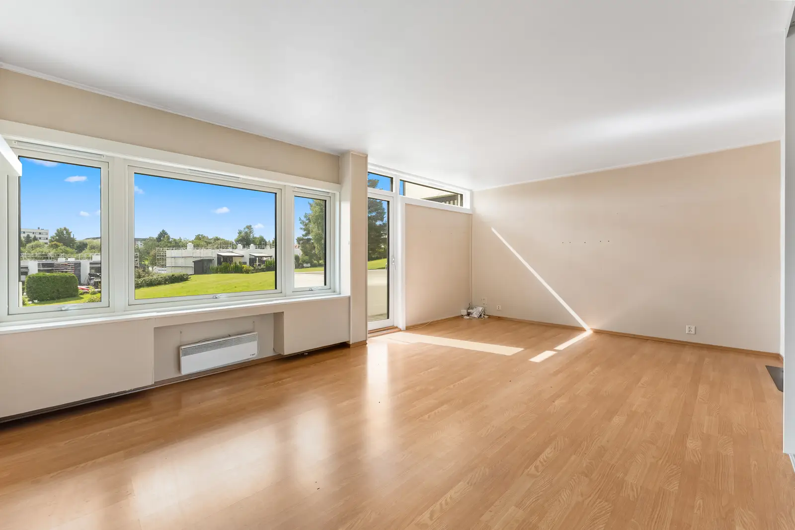 Stue med lysmalte veggflater og laminat på gulv. Store vindusflater slipper inn godt med dagslys og bidrar til en luftig romfølelse.