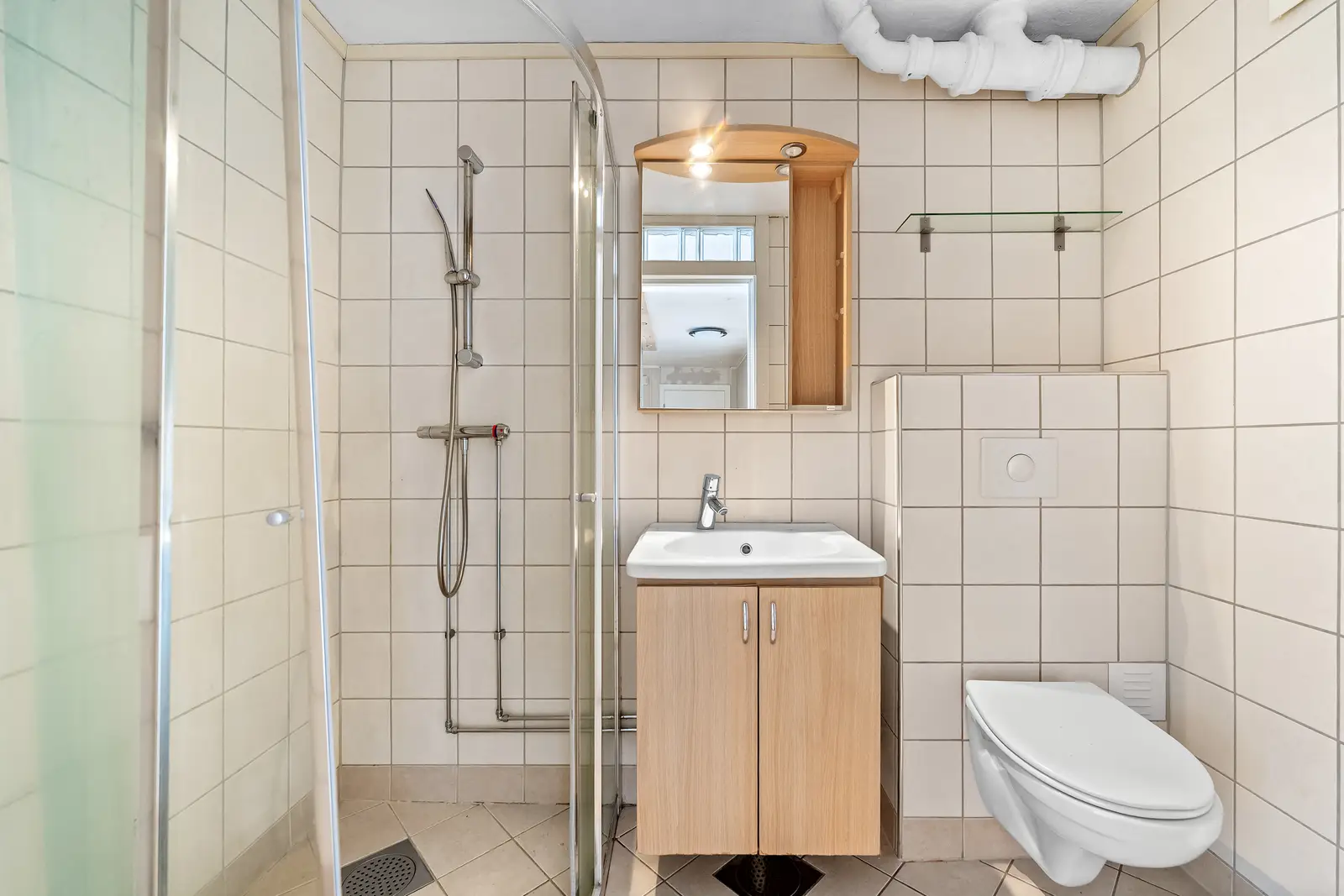 Flislagt bad av eldre dato (eksakt alder er ikke kjent). Badet er innredet med servantmøblement, speilskap, vegghengt toalett og separat dus